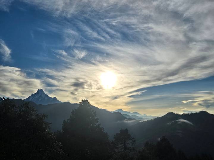 Dramatic sunrise over layered Himalayan peaks with the sun glowing through streaked clouds.