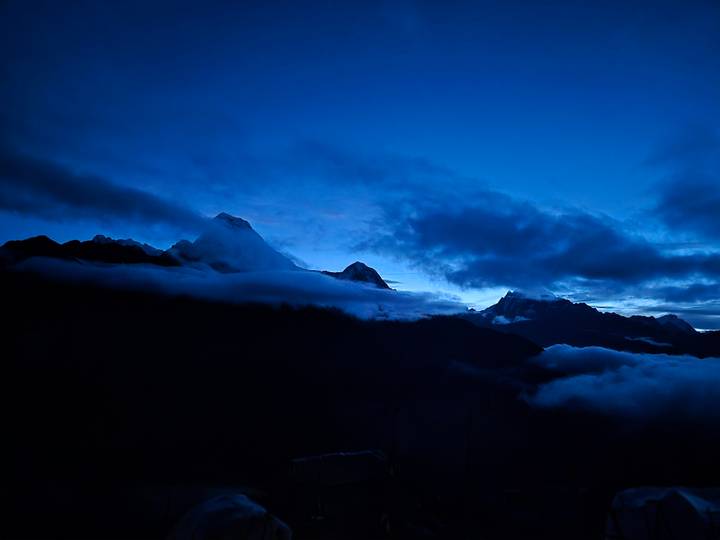 Blue hour silhouette of cloud-shrouded Himalayan peaks against a deep indigo sky.