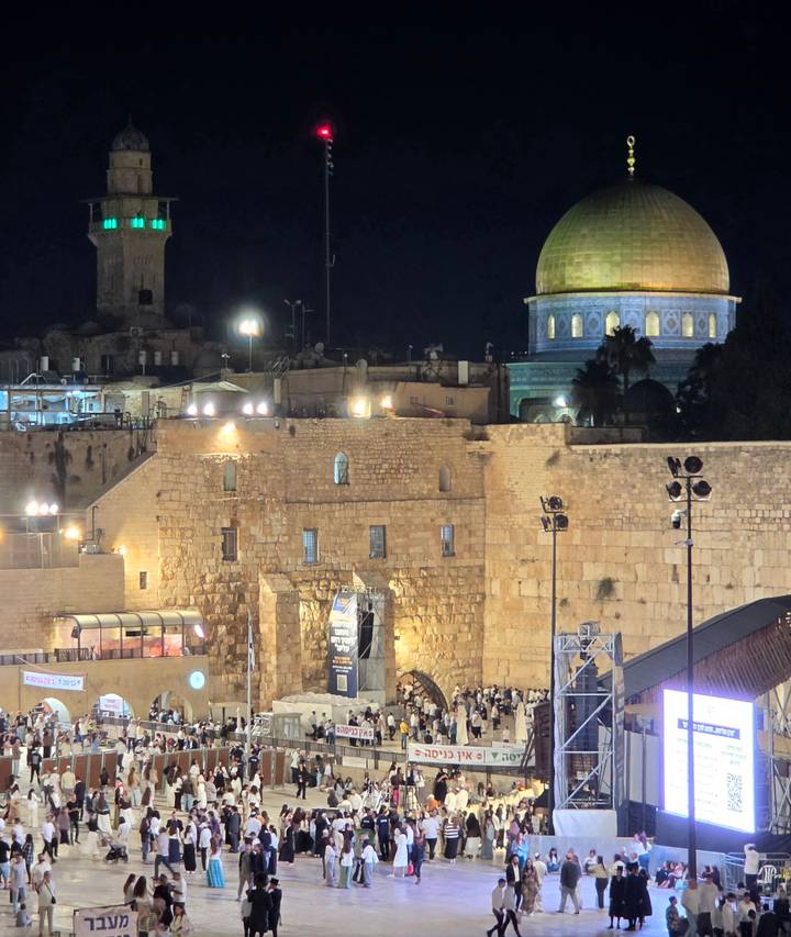 Night view of the Western Wall with the golden Dome of the Rock behind, illuminated against the dark sky.