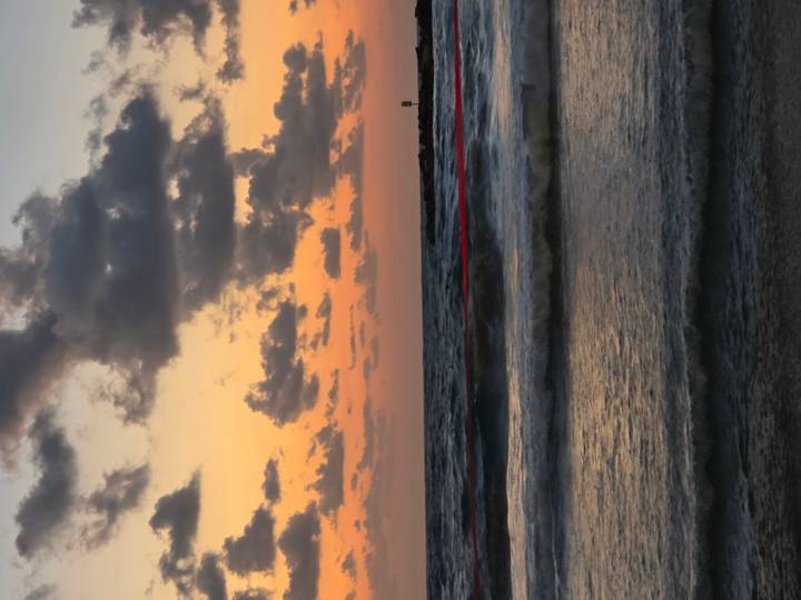 Vertical shot of waves rolling in under a dramatic orange and purple sunset sky.