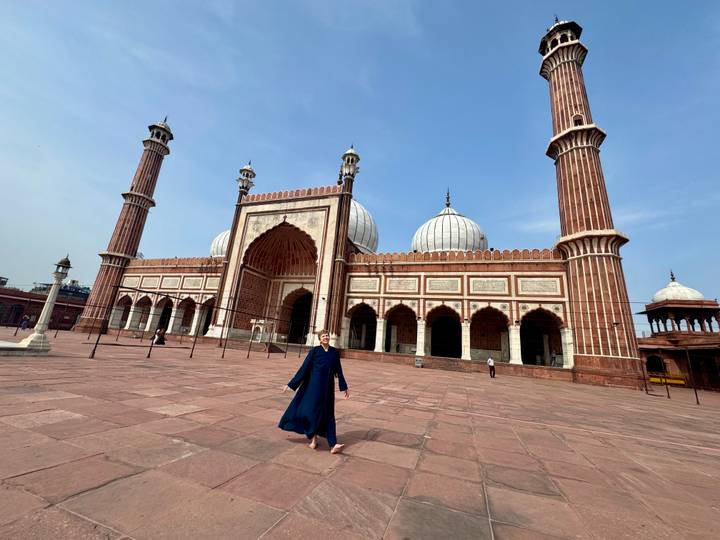 Traveller in blue robe walks barefoot across the courtyard of Jama Masjid with towering minarets.