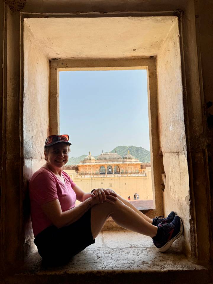 Traveller framed by sandstone archway overlooks ornate palace courtyard and distant green hills.