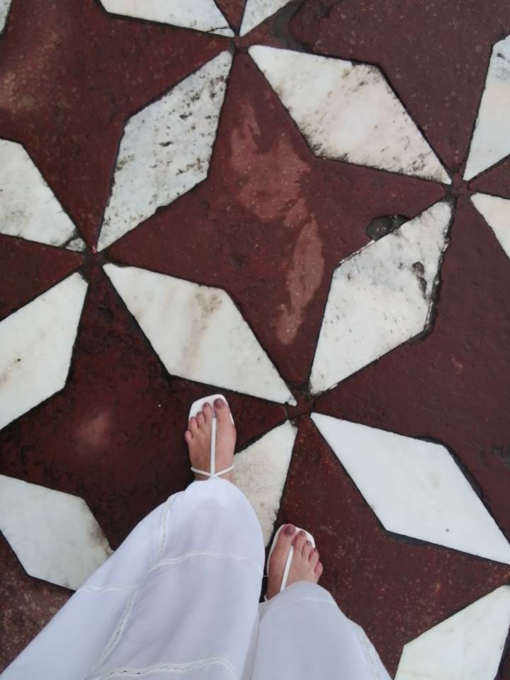 Close view of a sandal-clad foot on red and white marble floor tiles forming geometric shapes.