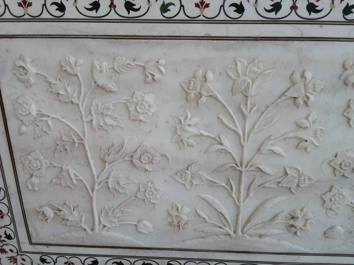 Detailed white marble relief carvings of flowers in the Taj Mahal.