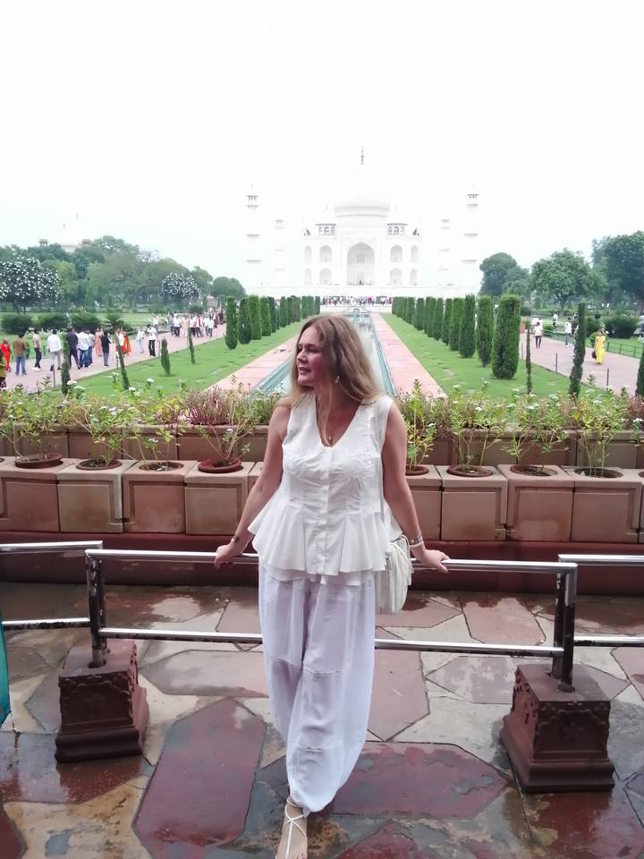 Woman posing on terrace with long water channel and Taj Mahal in the distance.