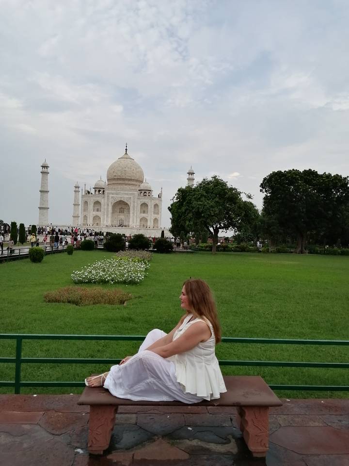 Woman stands in a green lawn area with full view of Taj Mahal behind.