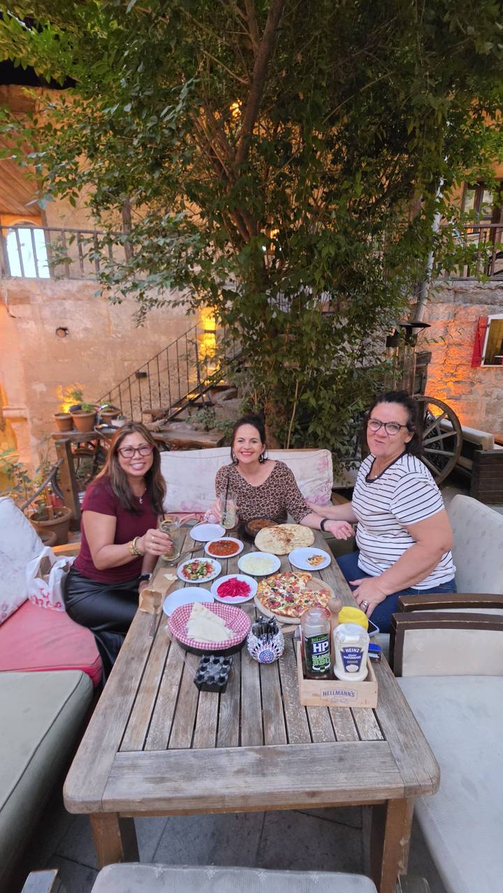 Three friends enjoy a Turkish meal at an atmospheric courtyard table surrounded by stone walls and warm lights.