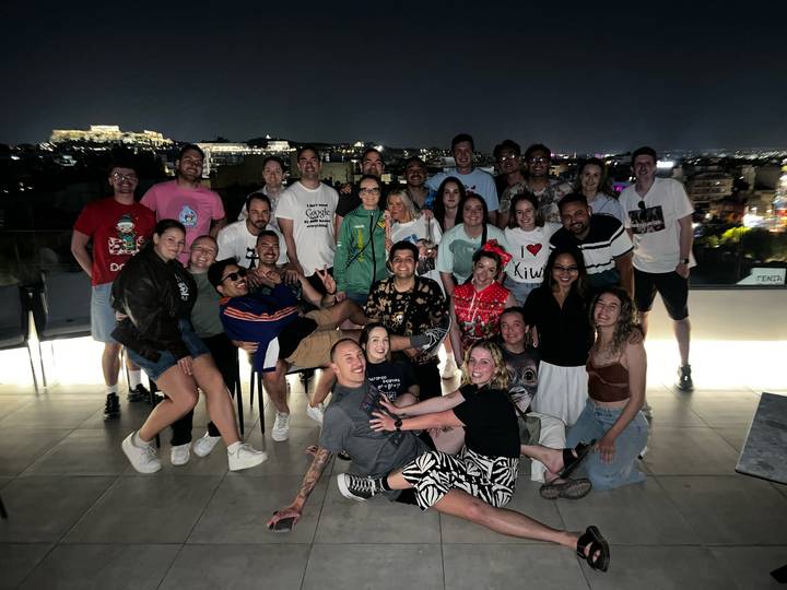 Large tour group posing on a rooftop terrace at night with the illuminated Acropolis visible in the distance.