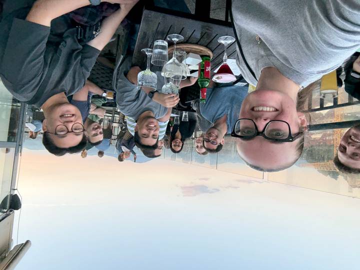 Friends enjoying drinks at an open-air rooftop bar during sunset with distant city and mountain views.