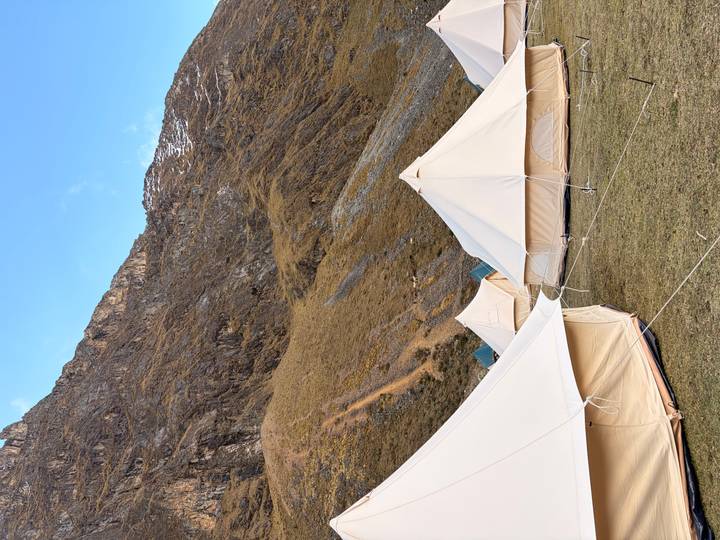 Series of cream canvas bell tents pitched on grassy terrain beneath rugged mountain slopes.