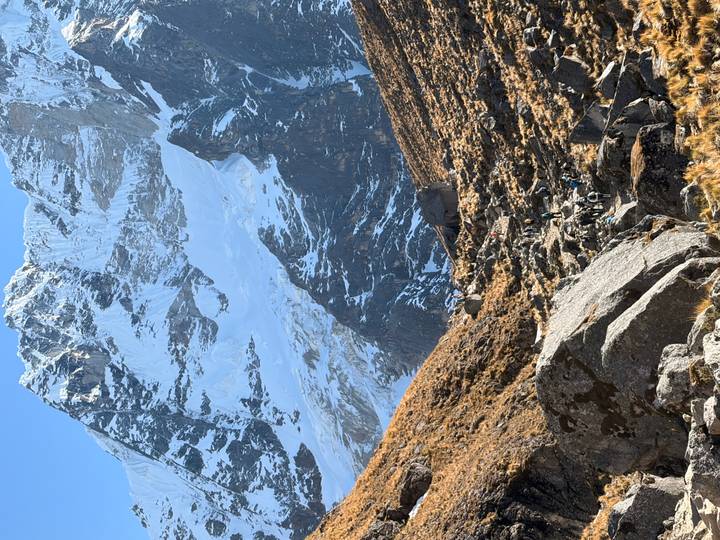 Steep Andean trail with hikers dwarfed by towering snow-clad peaks and rocky terrain.