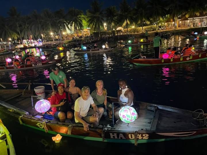 Travellers sit in a wooden boat on a lantern-lit river during Hoi An's colourful night market.