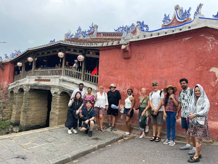 Large tour group poses before Hoi An's historic Japanese Covered Bridge on an overcast day.