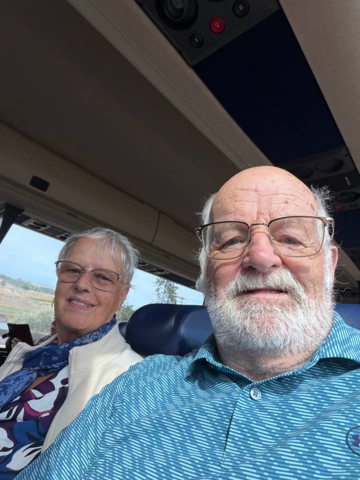 Selfie of older couple sitting on tour bus interior.