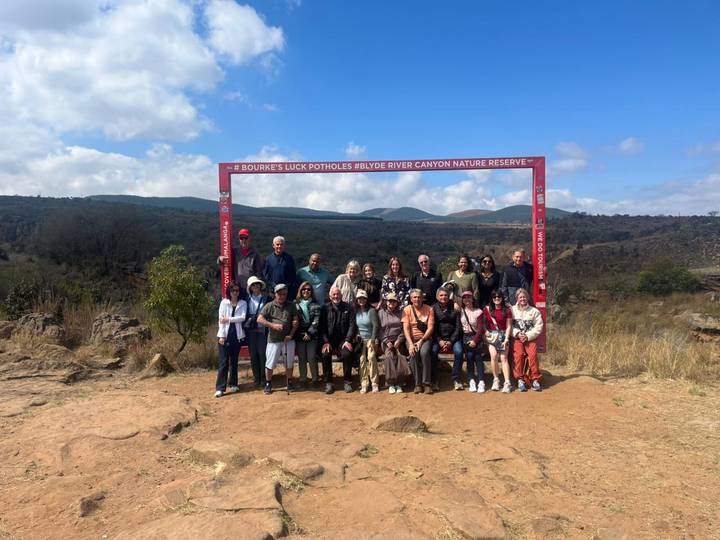 Large tour group poses under a red frame sign at Bourke’s Luck Potholes viewpoint.