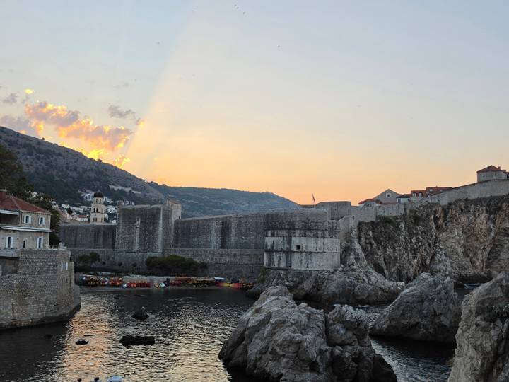Dubrovnik’s massive stone walls and fortifications glow under a pastel sunset sky.