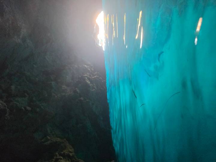 Turquoise blue water inside a sea cave with light streaming through the distant entrance.