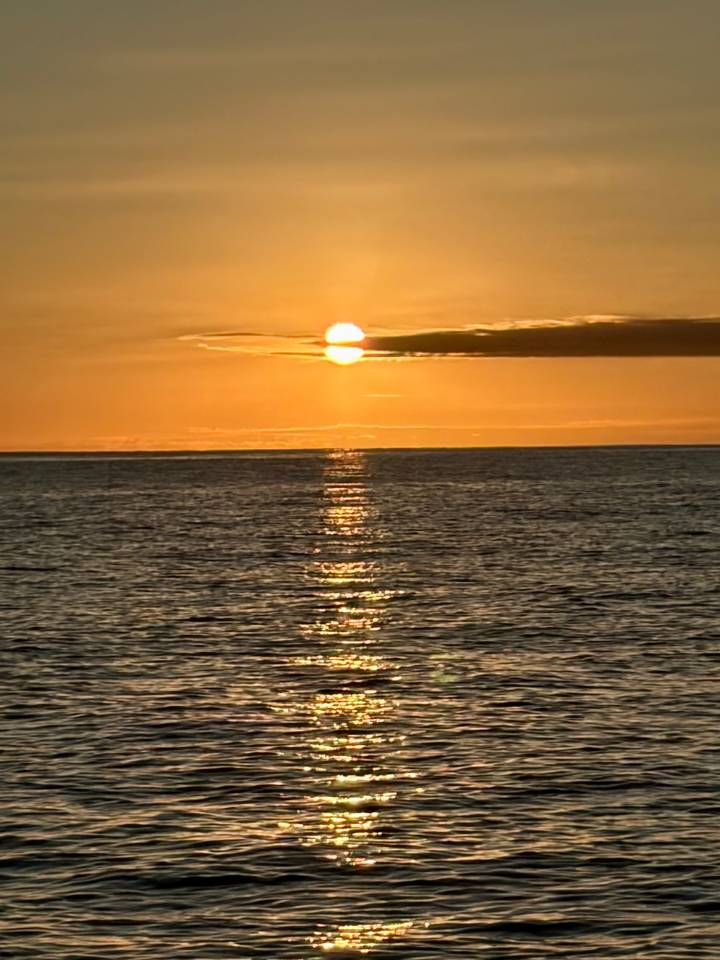 Golden sun sets over a calm ocean, casting a shimmering reflection on the water.