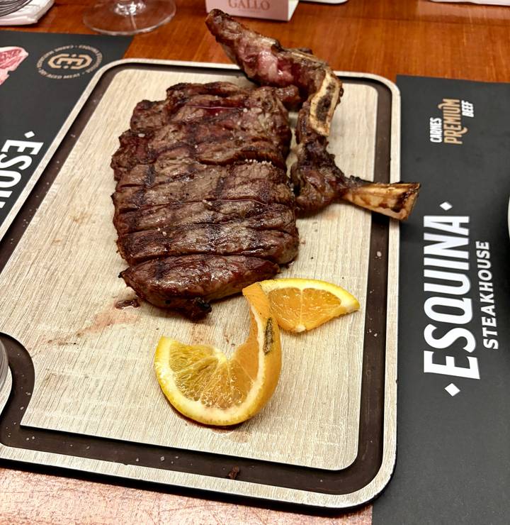 Grilled rib steak served on a wooden board with orange slices at a steakhouse.