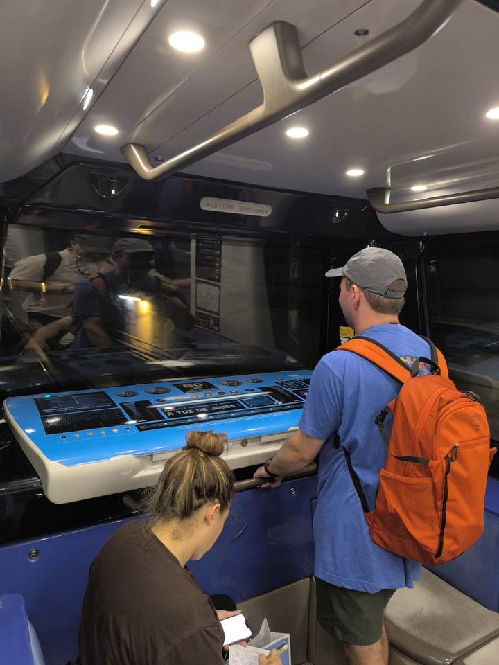 Man with orange backpack operates an interactive control panel at the front of a metro train.