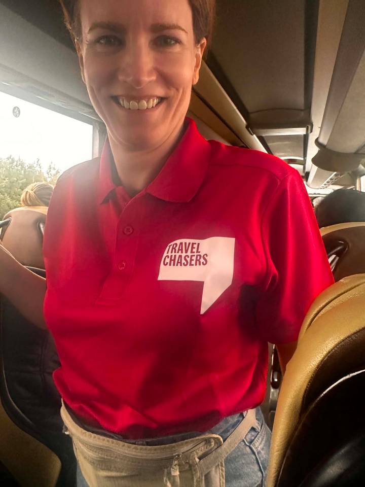 Close shot of a guide’s red polo shirt with the logo 'TRAVEL CHASERS' inside a tour bus.