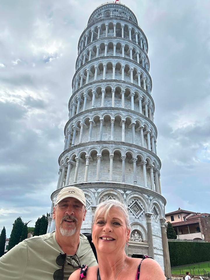 Traveler poses humorously in front of the Leaning Tower of Pisa under a cloudy sky.