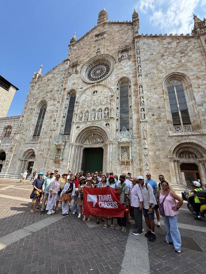 Large tour group posing with a banner in front of an ornate marble cathedral facade.
