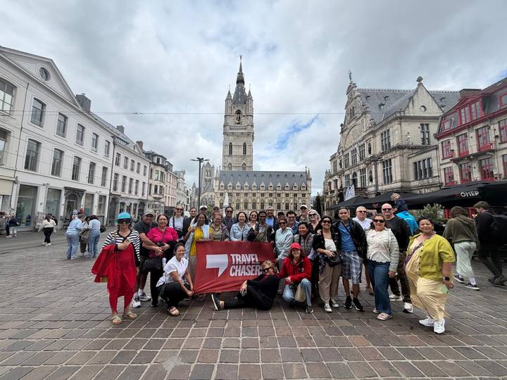 Tour group holding a red flag in a European square with a tall medieval belfry in the background.