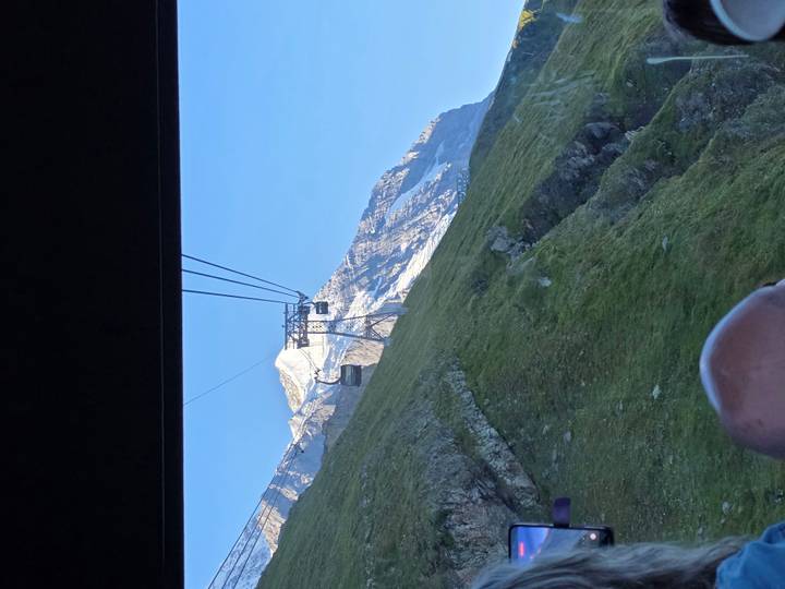 View from inside a cable car heading up toward a snow-capped Alpine peak.