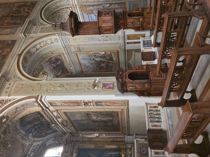 Richly decorated baroque church interior with frescoed ceilings, carved wood pulpit and benches.