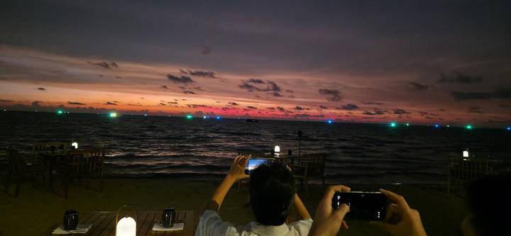 Beachside sunset with vivid colors while people capture the scene on their phones.