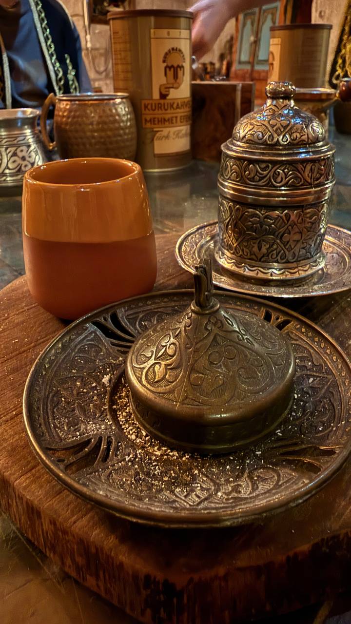 Ornate metal Turkish coffee set and a glass pot arranged on an intricately patterned tray in low warm light.