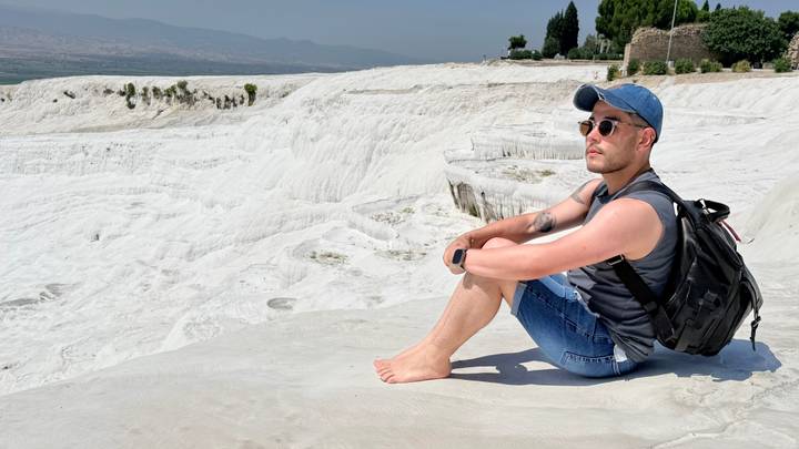 Barefoot traveler sitting on the white travertine terraces of Pamukkale looking over the landscape.