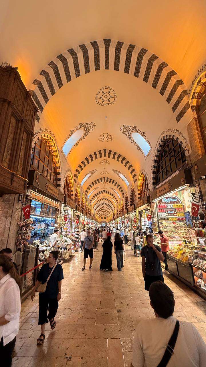 Busy interior of Istanbul’s Spice Bazaar with arched patterned ceiling and stalls glowing with warm lights.