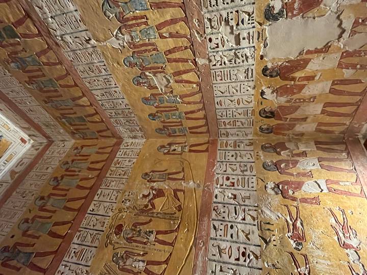 Vivid ancient wall paintings depicting Egyptian figures and hieroglyphs inside a royal tomb chamber.