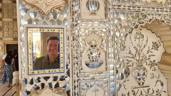 Traveler’s reflection framed by intricate mirror mosaics and marble in Jaipur’s Sheesh Mahal.