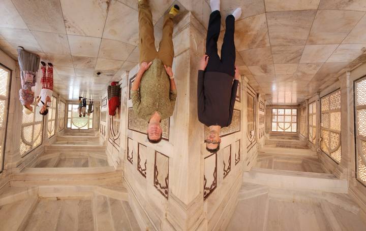 Two friends pose inside an airy marble corridor adorned with delicate lattice windows at a Mughal monument.