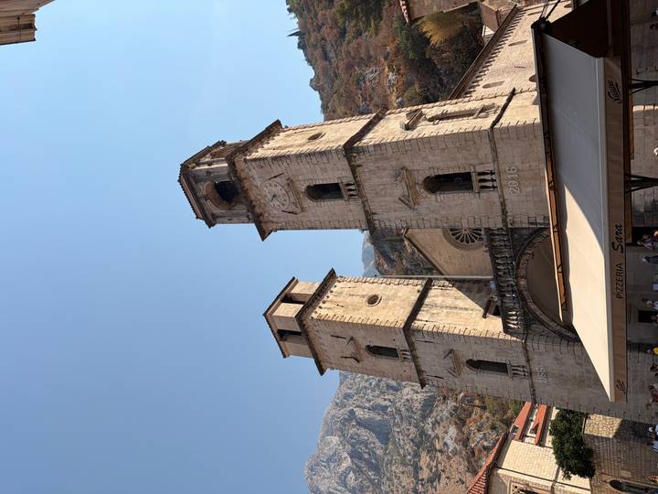 Twin stone bell towers of a historic cathedral stand against a clear blue sky and mountain backdrop.