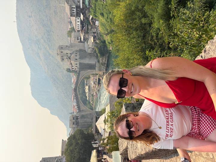 Two women pose in front of Mostar’s iconic stone arch bridge spanning a turquoise river.