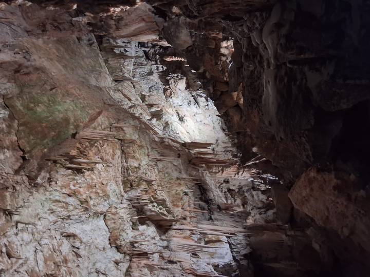 Dimly lit limestone cave interior with dramatic stalactites and jagged rock formations.