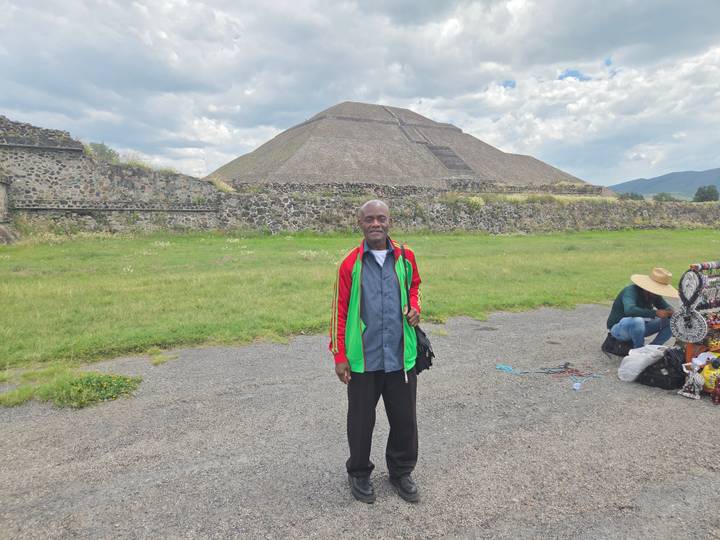 Visitor poses before the massive Pyramid of the Sun at Teotihuacan under a partly cloudy sky.
