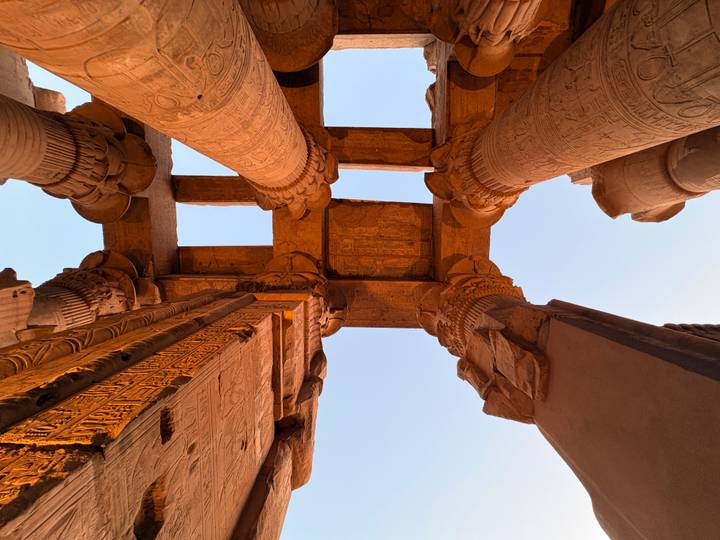 Symmetrical upward shot of colossal sandstone columns and lintels bathed in golden light.