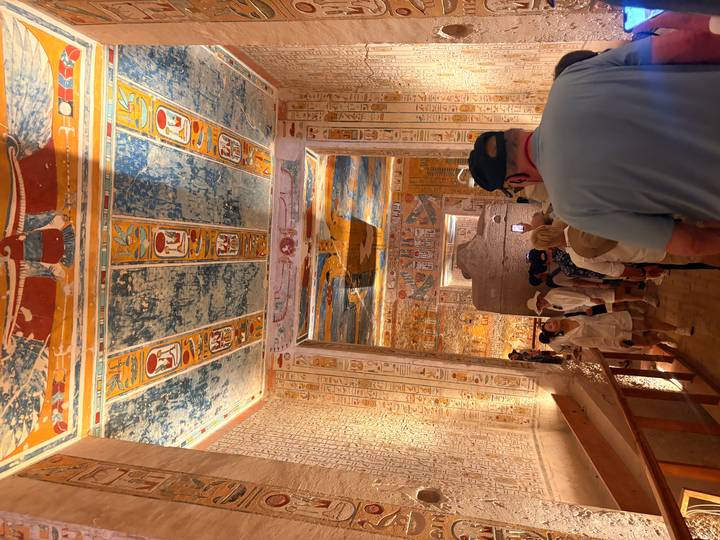 Tour group walking through a vividly painted tomb chamber with intricate hieroglyphic ceilings.