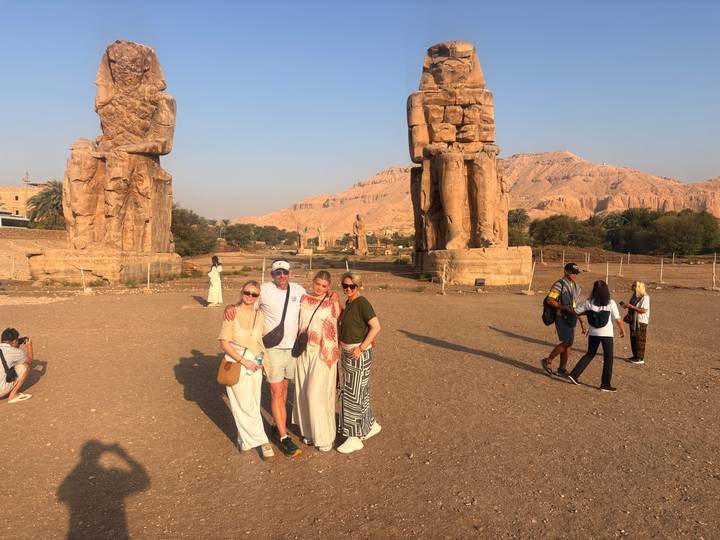 Travellers posing for a photo between the twin Colossi of Memnon statues with desert hills behind.