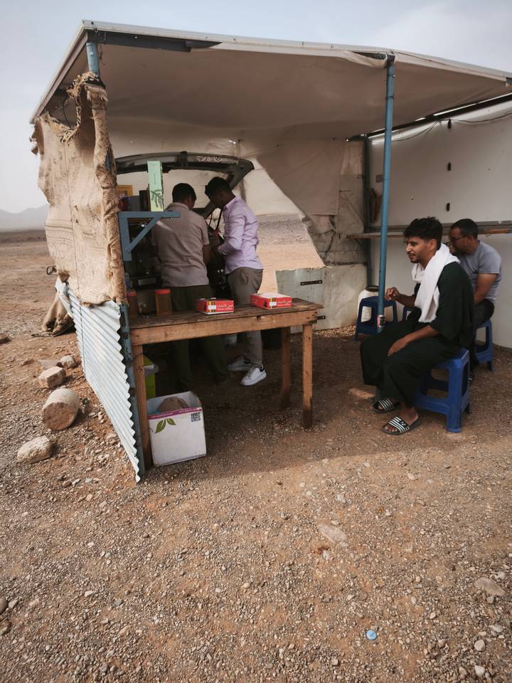 Simple roadside tea stall in a rocky desert with travellers sitting on plastic stools