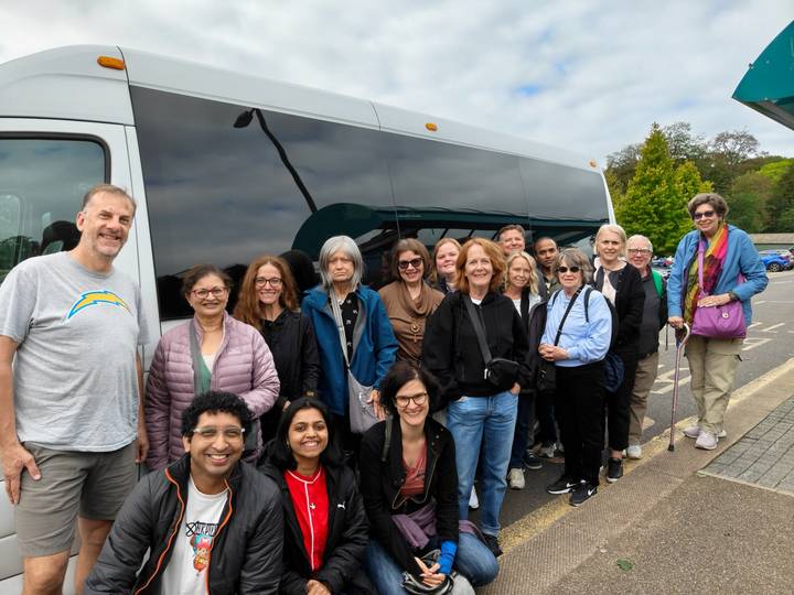 Large tour group smiling beside their white minibus on a roadside stop