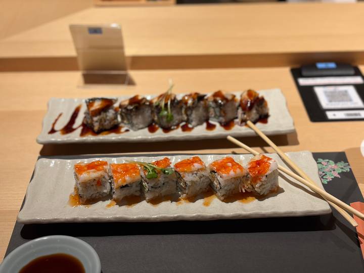 Artfully plated sushi rolls drizzled with sauce on ceramic trays with chopsticks