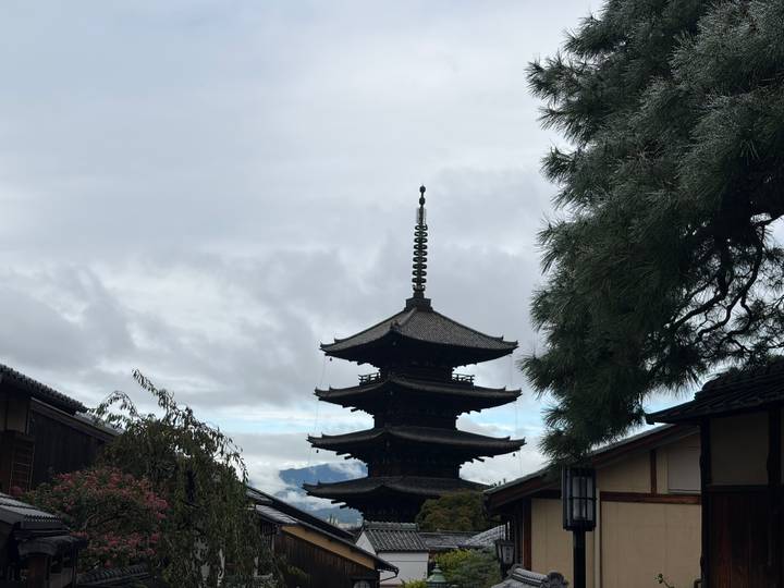 Five-storied wooden pagoda rising above traditional rooftops under a cloudy Kyoto sky