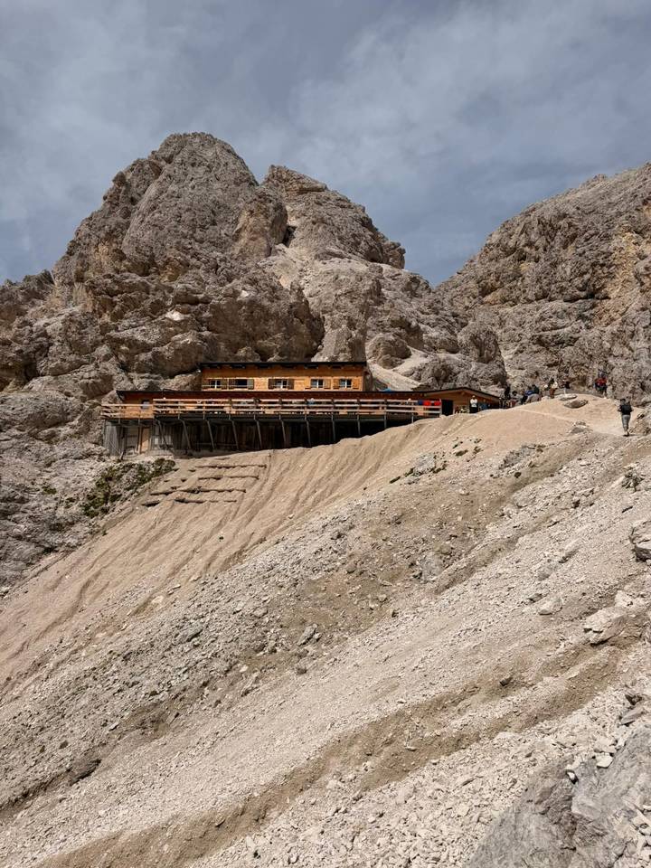 Mountain refuge hut perched on a scree slope surrounded by dramatic Dolomite cliffs