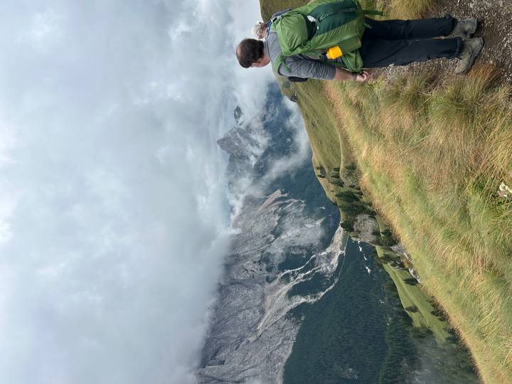 Hiker gazes over misty alpine valleys and jagged peaks from a grassy ridge
